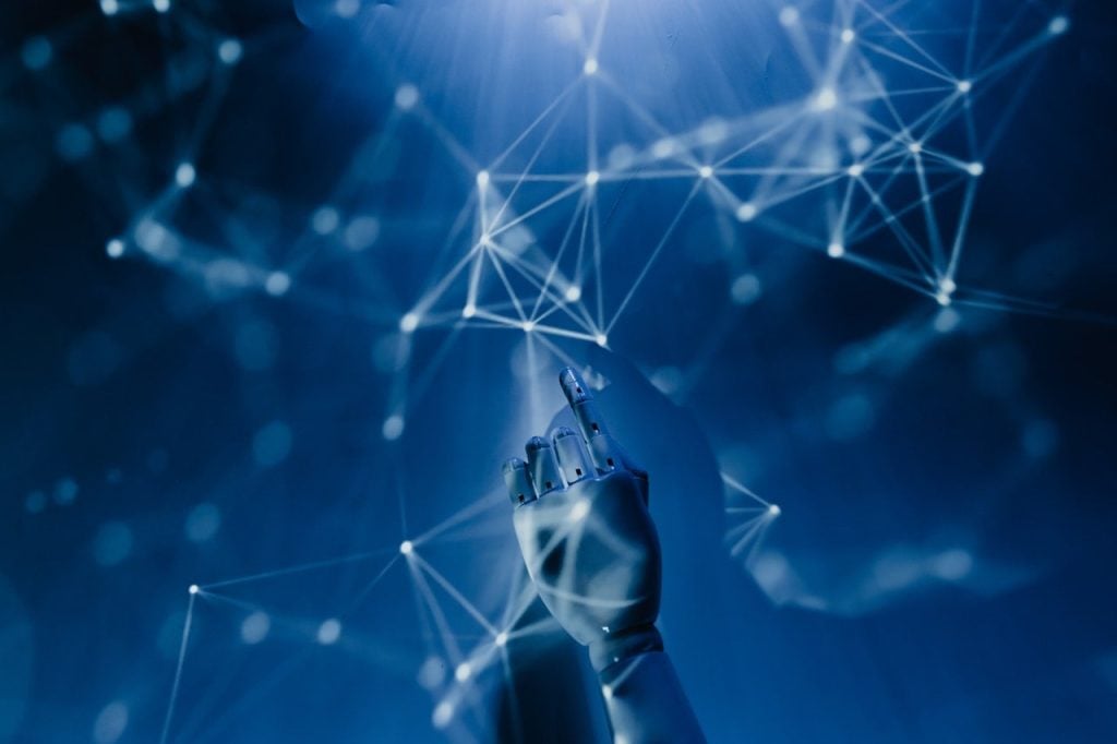 A robotic hand reaches upward toward a glowing network of interconnected nodes and lines, symbolizing adaptive therapy and the future of cancer therapy through advanced technology and artificial intelligence, against a blue-toned background.
